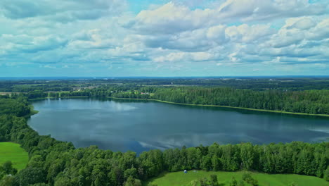 Lake-water-reflecting-cloudscape-surrounded-by-woodland,-aerial-view