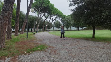 Lone-Woman-Strolling-On-City-Park-Line-With-Pine-Trees-In-Arezzo,-Tuscany-Italy
