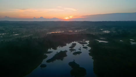 Early-morning-sunrise-over-misty-swamp-landscape,-aerial-view