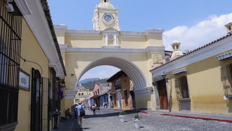 Touristen-Gehen-Auf-Der-Kopfsteinpflasterstraße-Unterhalb-Des-Santa-Catalina-Arch-In-Antigua,-GTM