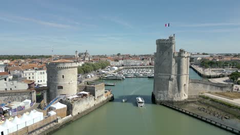 Cinematic-aerial-view-of-La-Rochelle-old-port-and-Saint-Nicolas-Tower-with-French-flag-waving,-France