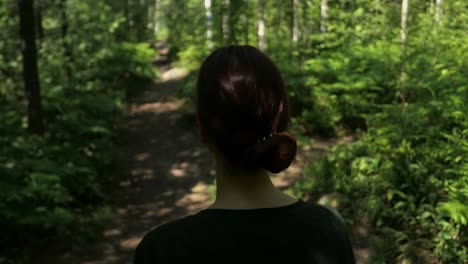 Woman-with-red-hair-walking-slowly-in-woods,-back-rear-view,-close-up