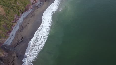 Luftaufnahme-Von-Weißen-Wellen,-Die-Am-Ufer-Der-Kupferküste-Waterford,-Irland,-Zusammenbrechen