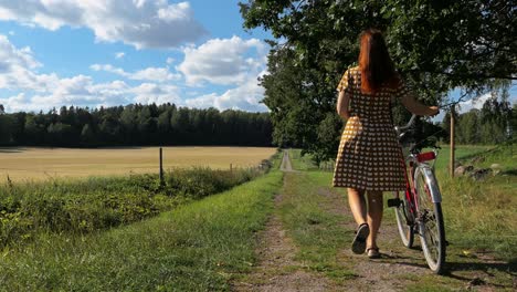 Woman-in-dress-walking-with-bicycle-country-road,-woman-vintage-dress-countryside