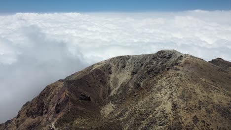 Volcano-crater-on-mountain-summit-in-sunshine-above-white-clouds
