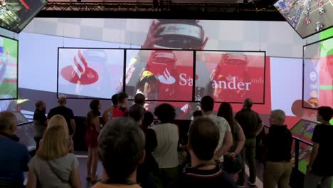 People-watch-a-montage-video-of-F1-Grand-Prix-winners-and-celebrations-during-the-history-of-the-sport-during-the-world's-first-official-Formula-1-exhibition-at-IFEMA-Madrid,-Spain