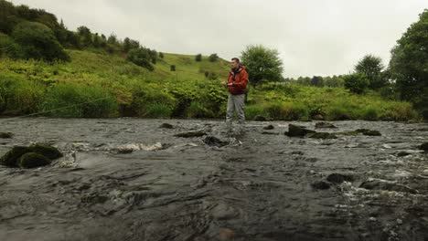 Toma-De-ángulo-Bajo-De-Un-Pescador-Con-Mosca-Lanzando-Y-Vadeando-En-Un-Pequeño-Río-En-Escocia.