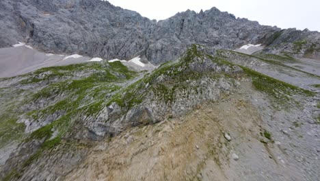Drone-flight-up-a-mountain-range-of-small-green-hills-and-a-steep-rocky-wall-in-Tyrol,-Austria