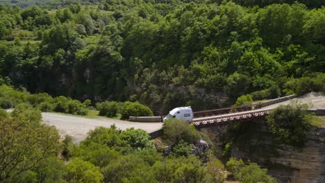 aerial-view-of-a-travel-caravan-over-the-bridge-on-a-sunny-day-over-Osumi-Canyon,-Albania