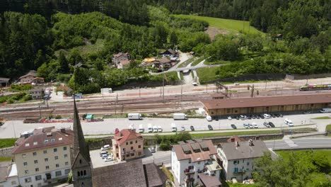 Cinematic-Aerial-Drone-shot-of-small-Italy-Village-between-Green-Mountains,-near-the-blue-Eisack-river-stream,-tall-bridge-and-train-station---Beautiful-Scenic-View