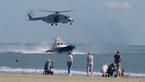 Zuschauer-Am-Strand-Schauen-Sich-Die-Übung-Der-Küstenwache-Mit-Rettungsboot-Und-Slomo-Des-Militärhubschraubers-NH-90-An