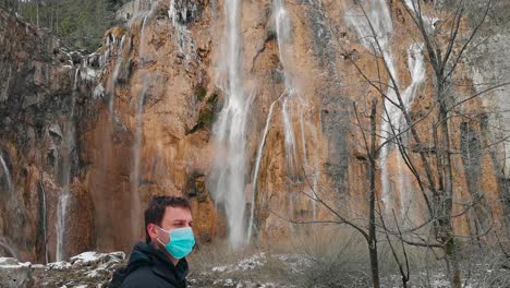 A-man-wearing-an-N95-mask-exemplifies-pandemic-safety-measures-against-the-backdrop-of-serene-natural-beauty,-with-gently-flowing-water-in-the-background-in-a-picturesque-Croatian-national-park