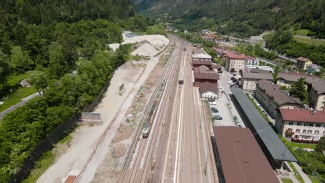 Vista-Aérea-Del-Tren-Sobre-Vías-De-Tren-En-Medio-De-Altas-Montañas-Verdes