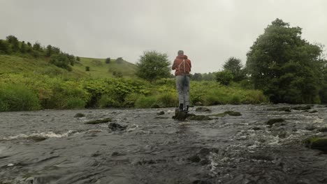 Hand-held-shot-of-a-fly-fisherman-standing-on-a-rock-casting-into-a-quick-river