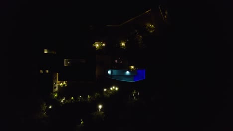 Aerial-ascending-shot-of-a-man-sitting-on-his-patio-at-night-in-his-villa