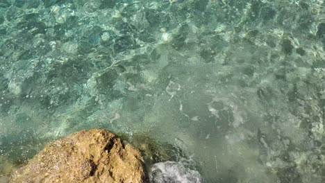 Felsige-Küste-Des-Mittelmeers-Mit-Kristallblauem,-Türkisfarbenem-Meerwasser-Und-Wunderschönem-Meeresboden-Mit-Felsen-Und-Kieselsteinen