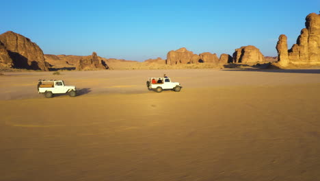 Aerial-view-over-a-4x4-full-of-people,-driving-in-sunlit-deserts-of-Saudi-Arabia