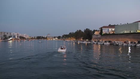 Small-powerboat-sailing-to-dock-during-nighttime-in-port-Zadar,-Croatia-with-city-vistas