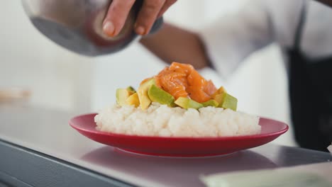 A-professional-chef-adds-salmon-and-soy-sauce-to-a-plate-with-avocado-and-rice,-preparing-a-sushi-dish,-traditional-Japanese-cuisine