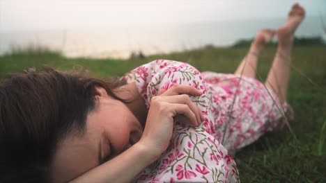 A-young-dark-haired-girl-in-a-dress-is-lying-on-the-grass,-smiling