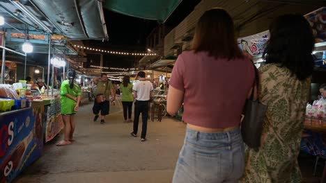 Tomando-Una-Panorámica-De-Izquierda-A-Derecha,-Se-Puede-Ver-A-Personas-Mirando-Y-Comprando-Comida-Y-Recuerdos-De-Los-Vendedores-Locales-En-El-Mercado-Flotante-De-Amphawa-En-Samut-Songkhram,-Tailandia.