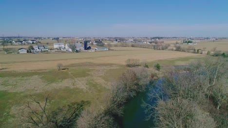 Eine-Drohnenansicht,-Die-An-Einem-Wintertag-Einem-Bach-Im-Herzen-Der-Amish-Landschaft-Folgt,-Der-An-Ackerland-Vorbeiführt