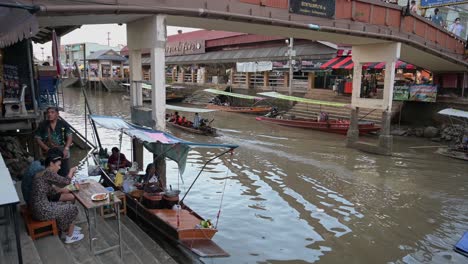 La-Cámara-Recorre-De-Derecha-A-Izquierda-A-Un-Grupo-De-Turistas-Cenando-Antes-De-Abordar-El-Tablero-Para-Su-Recorrido-Nocturno-Por-El-Mercado-Flotante-De-Amphawa-En-Samut-Songkhram,-Tailandia.