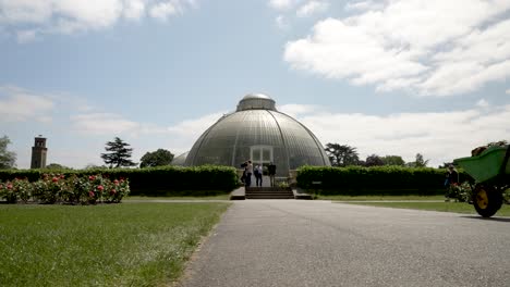 Camino-Que-Conduce-A-La-Entrada-Lateral-De-Palm-House-En-Kew-Gardens-Con-Gardner-Pasando-Con-Una-Carretilla-En-Un-Día-Soleado