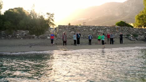 Eine-Gruppe-Von-Menschen,-Die-Yoga-Am-Malerischen-Strand-Machen,-4k,-Luftaufnahme
