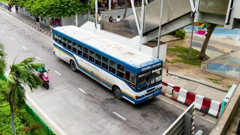 Aerial-View-Captures-a-Thai-Bus-at-a-Stop,-Surrounded-by-Passing-Traffic,-Pedestrians,-and-an-Outdoor-Escalator-in-Motion