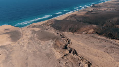 flying-over-cofete-beach,-fuerteventura:-aerial-view-traveling-out-to-the-great-mountains-and-the-beautiful-beach