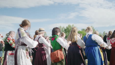 Gruppe-Von-Menschen-In-Traditioneller-Schwedischer-Kleidung,-Die-Während-Der-Mittsommerfeier-Auf-Einem-Feld-Mit-Der-Schwedischen-Flagge-Spazieren-Gehen