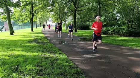 Grupo-Deportivo-En-Cámara-Lenta-De-Personas-Corriendo-En-Un-Maratón-De-Caridad-En-Un-Parque-Público-Sombreado