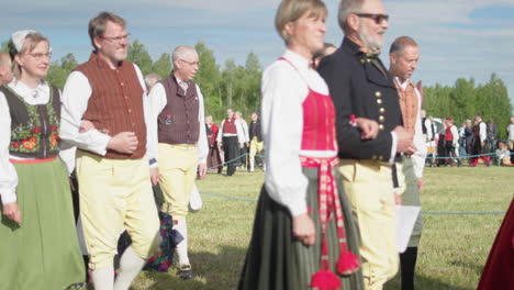 Grupo-De-Personas-Vestidas-Con-Ropa-Tradicional-Sueca-Caminando-En-Un-Campo-Para-Un-Evento-De-Celebración-De-Verano