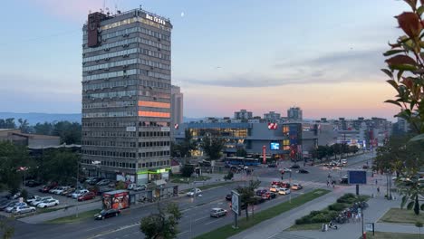 Novi-Sad,-Serbien,-Sehr-Belebte-Kreuzung-Mit-Fahrenden-Autos,-Bussen,-Fahrrädern,-Motorrädern-Und-Menschen-In-Der-Nähe-Von-Mercator-Und-Promenade,-Sonnenuntergang