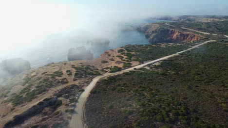 Flyover-clouds-of-fog-toward-scenic-Rocky-coastline-in-Portugal-Southeast