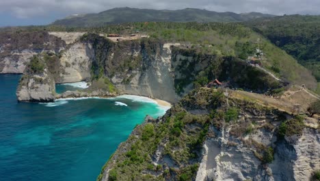 Soar-above-Diamond-Beach,-Nusa-Penida,-Bali,-our-exceptional-aerial-stock-footage,-Discover-Diamond-Beach-With-its-ivory-sands,-crystalline-waters,-iconic-rock-formations,-true-tropical-paradise