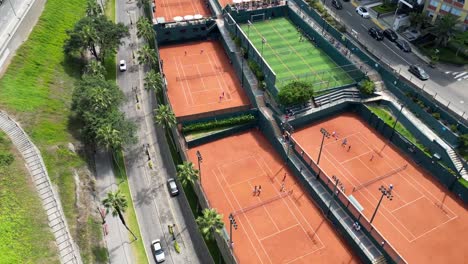 Stunning-tennis-club-discovered-by-an-aerial-drone-tilt-down-shot-in-the-middle-of-buildings,-palms,-trees,-historic-street-and-gardens