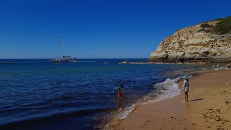 Kids-Playing-Together-On-Beautiful-Sandy-Beach-Near-Big-Rock,-Benagil,-Portugal