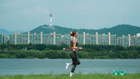 Woman-in-Sport-Clothes-Doing-Cordless-Jump-Rope-Exercises-Jumping-on-One-And-Both-Legs-at-Public-Hangang-Park-with-Famous-N-Seoul-Namsan-Tower-and-Mountain-View-in-Background-on-Hot-Summer-Day