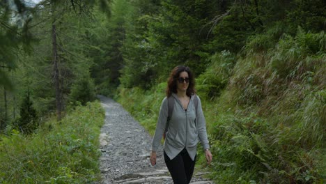 Woman-wearing-sunglasses-and-backpack-walks-on-mountain-trail-in-Alpe-ventina