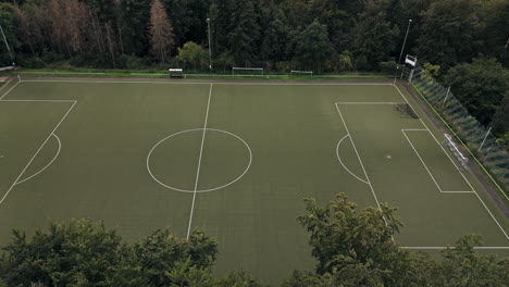 Aerial-Flight-besides-an-empty,-green-football-field-in-the-middle-of-the-forest,-Drone-Footage