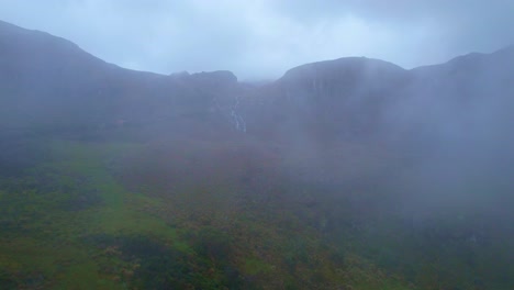 Luftaufnahme-Der-Berge-Des-Cajas-Nationalparks-In-Cuenca,-Ecuador,-Durch-Die-Wolken-Und-Mit-Blick-Auf-Einen-Wasserfall-Auf-Einem-Der-Berge-Im-Höchsten-Teil-Des-Parks