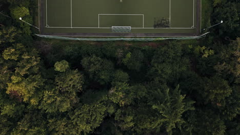 Luftaufnahme-Von-Oben-Nach-Unten-Auf-Das-Grüne-Fußballfeld-Mitten-Im-Wald,-Drohnenflug-Darüber,-Mit-Sonne-Und-Schatten
