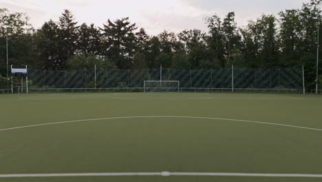 Mit-Einer-Drohne-über-Das-Gras-Eines-Grünen-Fußballfeldes-Fliegen,-Luftaufnahmen,-Fußballplatz,-Wald-Drumherum