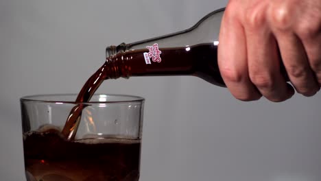 Real-Sugar-Coke-Coda-Been-Poured-into-Drinking-Glass-with-Ice-on-Grey-Background