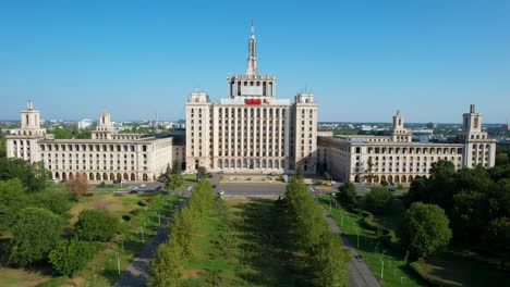 Aerial-View-Of-The-House-Of-The-Free-Press-Building-In-Bucharest,-Romania,-Surrounded-By-Green-Vegetation,-Sunrise,-Clear-Blue-Sky