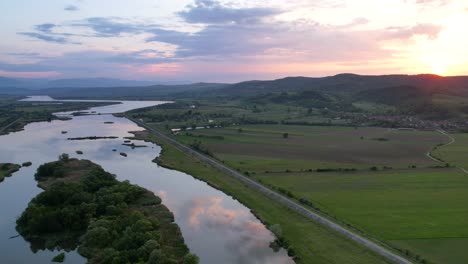 Hyperlapse-drone-shot-at-sunset-over-large-Olt-river-in-Transylvania-rural-area-with-green-grass-meadows-4K-aerial-video