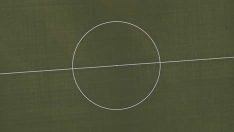 Top-Down-View-with-rotation-of-an-empty,-green-football-field-in-the-middle-of-the-forest,-Drone-Footage