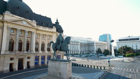 Vista-Aérea-Giratoria-De-La-Estatua-Del-Rey-Carol-I-De-Rumania-Frente-A-La-Biblioteca-De-La-Universidad-Central-En-La-Avenida-Calea-Victoriei,-Bucarest